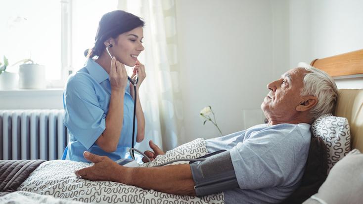 a nurse speaking to an older man who is laid in a bed